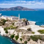 Donald Trump frente a un micrófono anunciando la reapertura de la prisión de Alcatraz, con vistas a la isla y la costa de San Francisco al fondo.