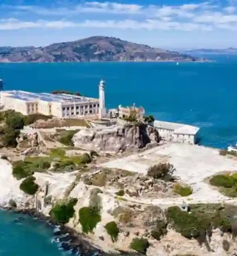Donald Trump frente a un micrófono anunciando la reapertura de la prisión de Alcatraz, con vistas a la isla y la costa de San Francisco al fondo.